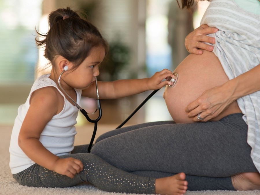 Kleinkind hört den Babybauch der Mutter ab. Schwangerschaft, Neuzuwachs, Familie, Geburt, Eltern - Canva