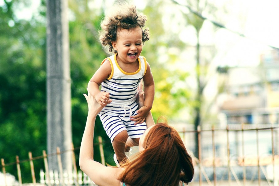 Junge Frau spielt mit einem lachenden Kleinkind, sie wirft es leicht hoch und fängt es wieder auf. Kindertagespflege, Adoption, Pflegefamilien, Pflegeeltern, - Photo by Thiago Cerqueira on Unsplash