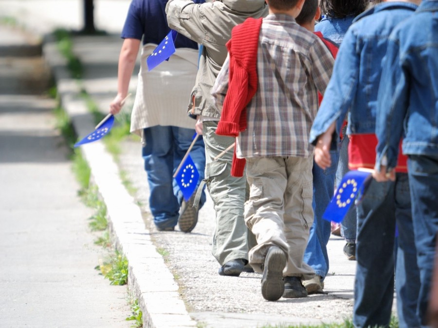 Erwachsene und Kinder laufen mit kleinen Europa-Fähnchen an einer Straße entlang. Die diesjährige Europawoche des Landes NRW steht unter dem Motto: eunited-gemeinsame Vision für die Zukunft - Canva