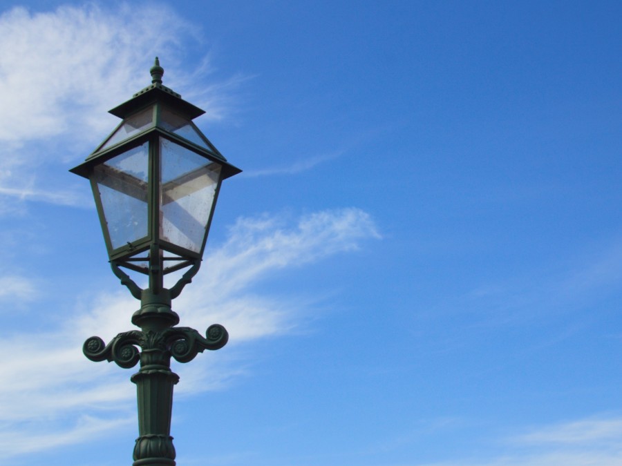 Straßenbeleuchtung, Laternen, Leuchten: Das Foto zeigt den oberen Teil einer alten Straßenlaterne vor blauem Himmel - Canva