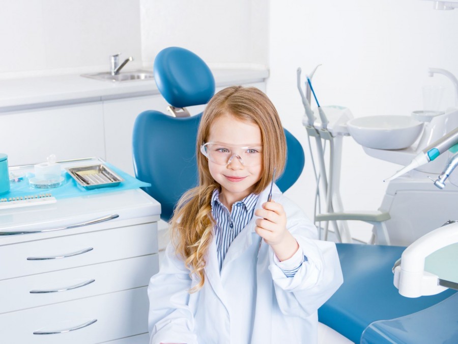 Ein lachendes Mädchen sitzt vor einem Zahnarztstuhl mit einem Instrument in der Hand in einer Zahnarztpraxis. - Gesundheitsamt - Canva von monst Arrrr
