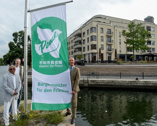 Flagge zeigen gegen Atomwaffen - Oberbürgermeister Ulrich Scholten (rechts) hisst am Stadthafen die Flagge gegen Atomwaffen. 184 Städte und Mayors for Peace machen bei der Aktion mit. Stadthafen. 08.07.2016 Foto: Walter Schernstein