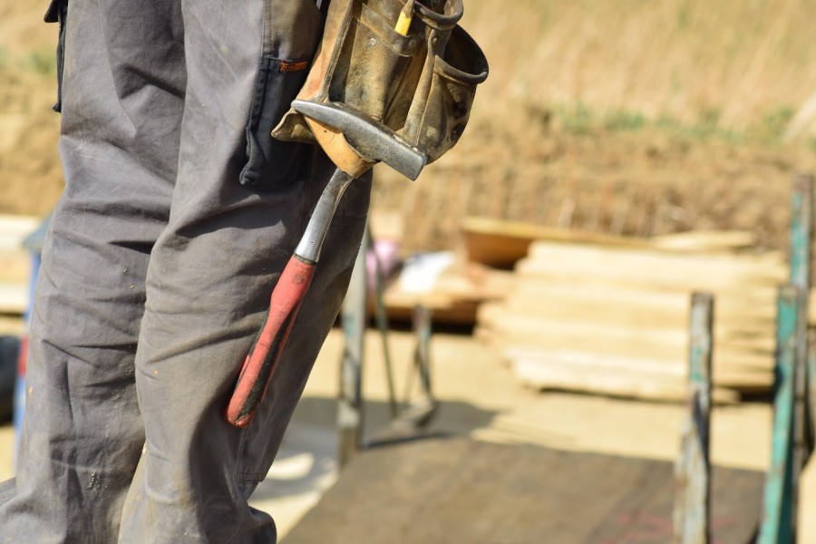 Bildauschnitt aus einer Baustelle: Beine eines Handwerkers mit Werkzeuggürtel an dem ein Hammer hängt. Informationen zum Handwerkerparkausweis. - Bild von annawaldl auf Pixabay