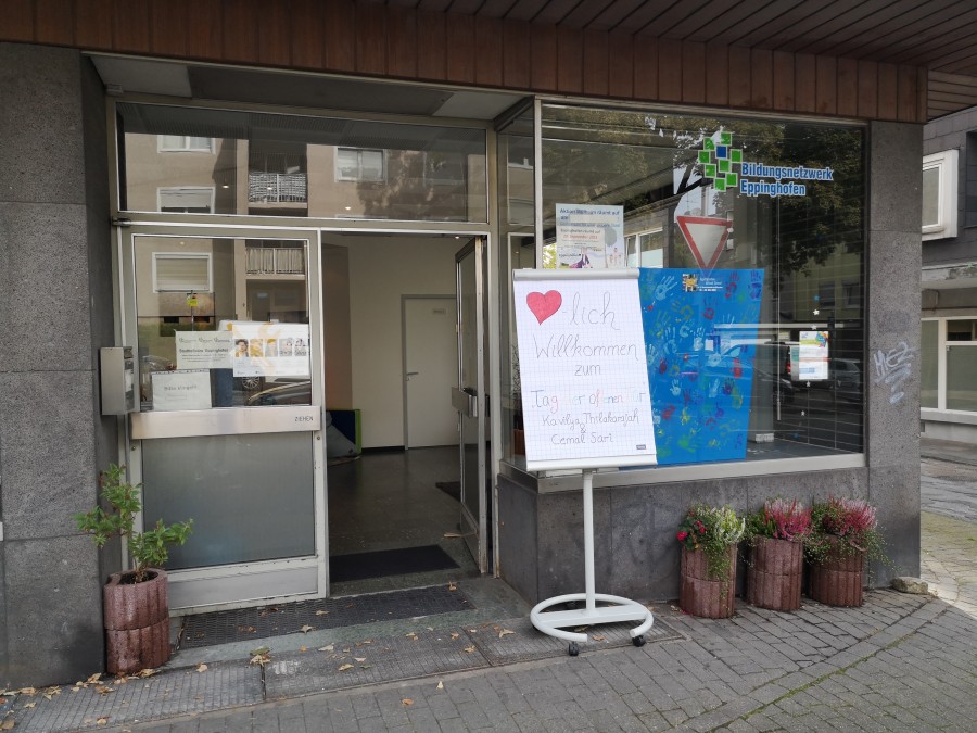 Die Eingangstür des Stadtteilmanagements Eppinghofen und das einladende Schild mit dem Blumenkübel vor dem Stadtteilbüro. - Cemal Sari