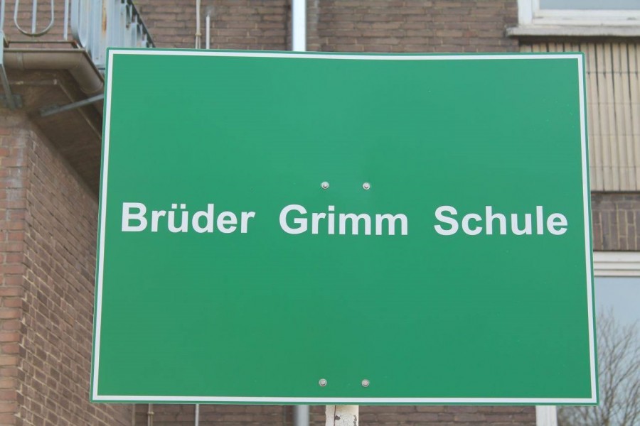 Schild der Grundschule Brüder Grimm vorm Schulgebäude (weiße Schrift auf grünem Hintergrund) - Brüder Grimm Schule