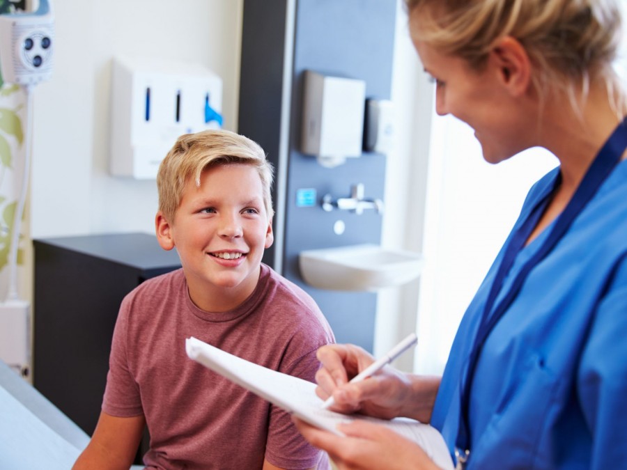 Ein blonder Junge in einem roten Shirt sitzt bei einer blonden Ärztin für ein Beratungsgespräch. - Gesundheitsamt - Canva von Monkey Business Images