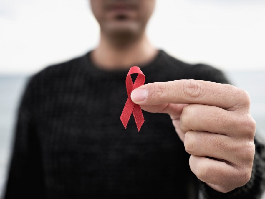 Ein Mann mit einem schwarzen Pullover hält eine rote Aidsschleife in die Kamera. - Gesundheitsamt - Canva von Juan Moyano