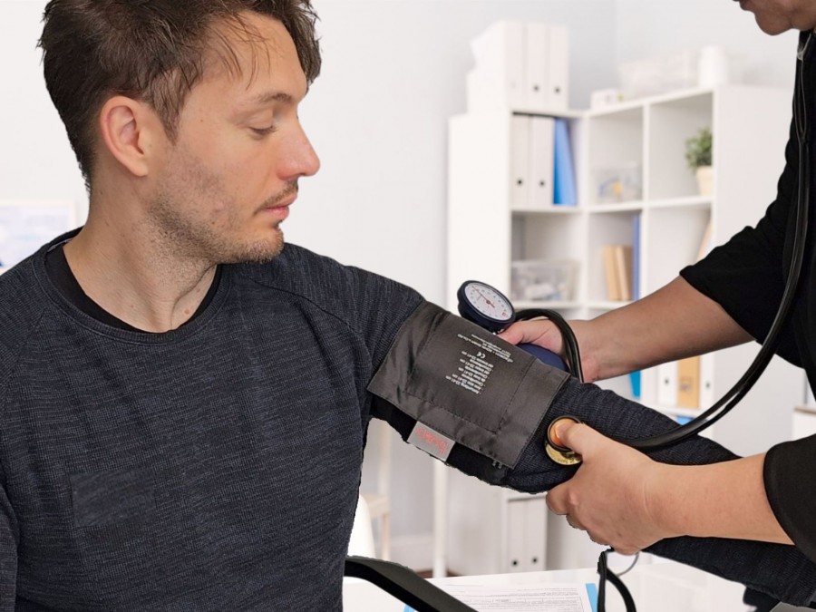 Ein Mann lässt sich von einer Ärztin Blutdruck im Behandlungszimmer messen - Gesundheitsamt - F. Fedtke