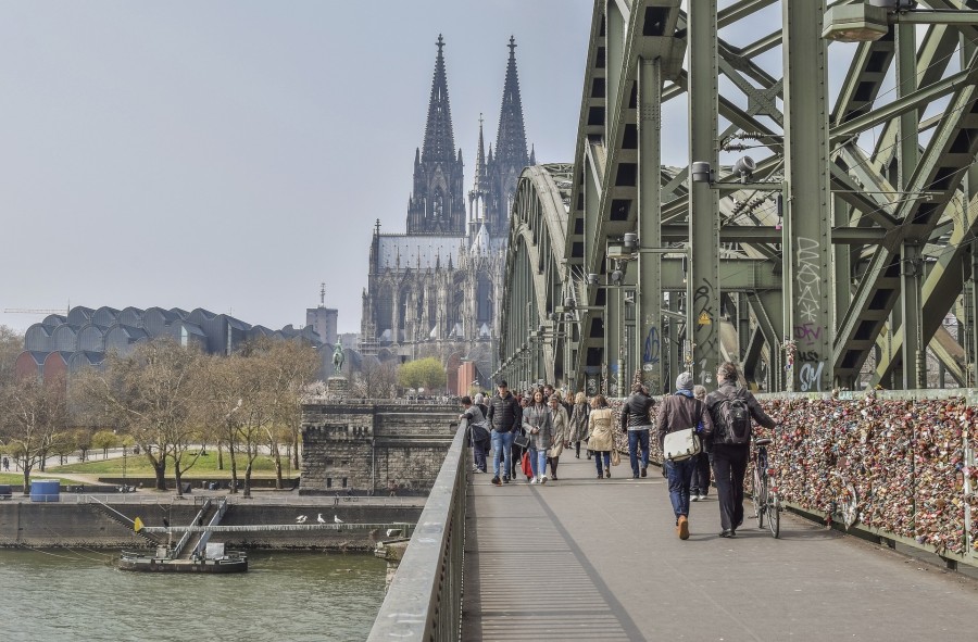 Blick über die große Rheinbrücke auf den Kölner Dom. An den Gitterzäunen mit den Liebesschlössern vorbei spazieren Menschen über die Brücke. - Bild von https://500px.com/ michael-gaida auf Pixabay