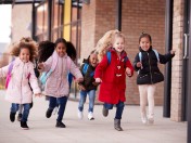 Mehrere Grundschulkinder rennen mit ihren Schultaschen auf dem Rücken lachend an der Schule vorbei. Grundschulen, Einschulung, 