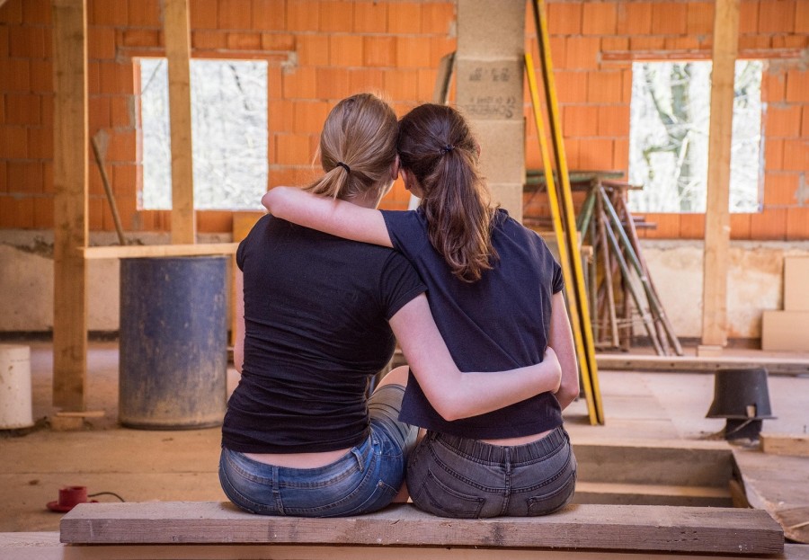 Zwei Frauen sitzen mit dem Rücken zur Kamera, Arm in Arm, auf einer Bank und schauen in einen Raum in ihrer Immobilie, der gerade kernsaniert wird.  - Pixabay