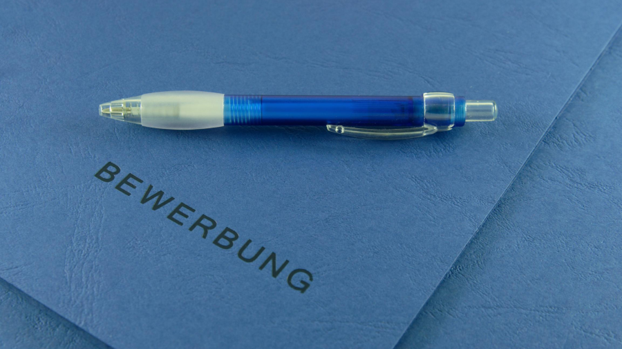 Kugelschreiber auf blauer Bewerbungsmappe. Stellenangebote, Jobcenter, Bewerbungsgespräch, U25 - Canva