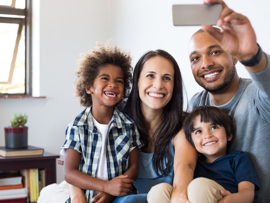 Familie mit zwei Kindern machen zuhause ein Selfi und lachen in die Kamera. Mutter, Vater, Pflegeeltern, Adoption, - Canva Familie mit zwei Kindern machen zuhause ein Selfi und lachen in die Kamera. Mutter, Vater, Pflegeeltern, Adoption, - Canva