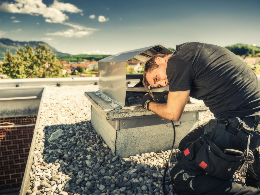Schornsteinfeger auf einem Hausdach bei der Überprüfung eines Schornsteines. Heizungsanlagen und Schornsteine sollten regelmäßig von Fachleuten überprüft werden. - Canva