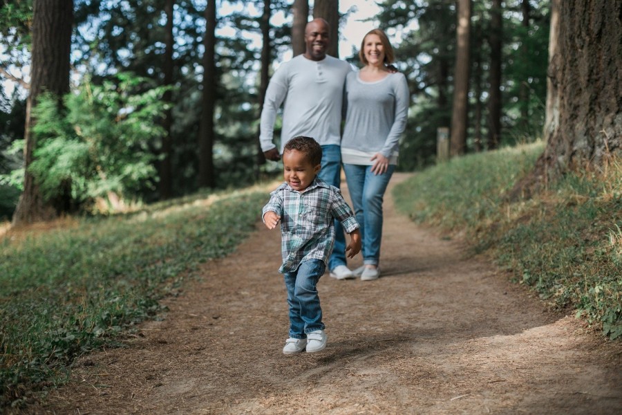 Familie macht einen Spaziergang im Wald, das Kleinkind rennt voraus und die Eltern laufen Arm in Arm hinterher. Eltern, Adoption, Pflegekind, Pflegefamilien - Bild von Brad Dorsey auf Pixabay