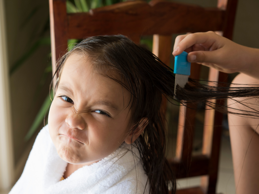 Junges Mädchen schaut genervt und grimmig in die Kamera, ohre Haare und Kopfhaurt werden auf Kopfläuse untersucht. Gesundheitsaufsicht - Canva