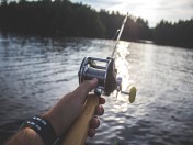 Hand die eine Angelrute am Wasser festhält. Stichwörter: Angeln, Fischerei, Fischerprüfung, Angelschein