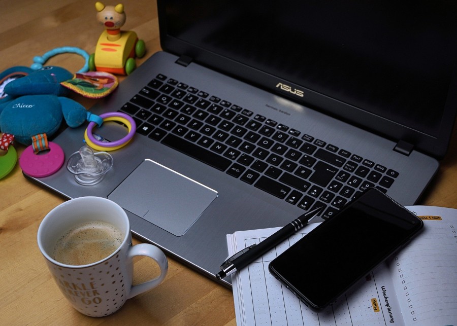 Vereinbarkeit von Familie und Beruf - Auf dem Tisch steht ein Laptop, ein Handy, eine Kaffeetasse und Baby Spielzeug.   