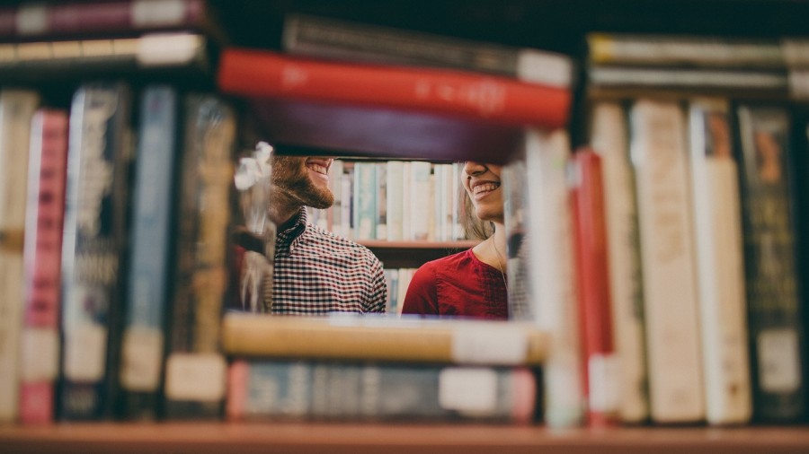 Sicht durch ein Bücherregal: Schülerin und Schüler in der Bibliothek. Schulraktika, Praktikum, Studium, Studierende, Ausbildung - Pixabay