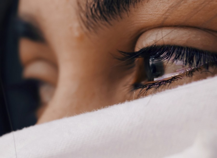 Bildausschnitt, tränengefüllte Augen einer Frau, mit weißem Tuch vor Mund und Nase.  Symbol für Zwangsheirat. Gleichstellungsstelle - Photo by Luis Galvez on Unsplash