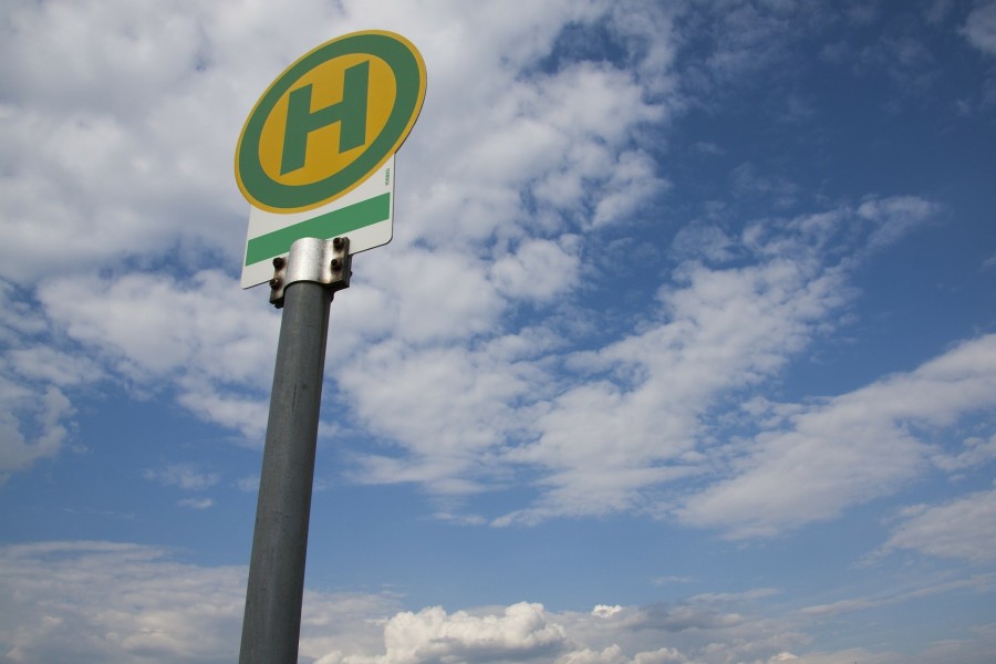 Das Foto zeigt ein rundes Haltestellenschild des Öffentlichen Personennahverkehrs mit einem grünen H auf gelbem Hintergrund (Ruhrbahn, VRR, Busse, Bahnen, Trams) vor blauem Himmel mit weißen Wolken. Umweltschutz, Feinstaub, CO2-Wert, Abgase, Klimafreundlich. - Pixabay