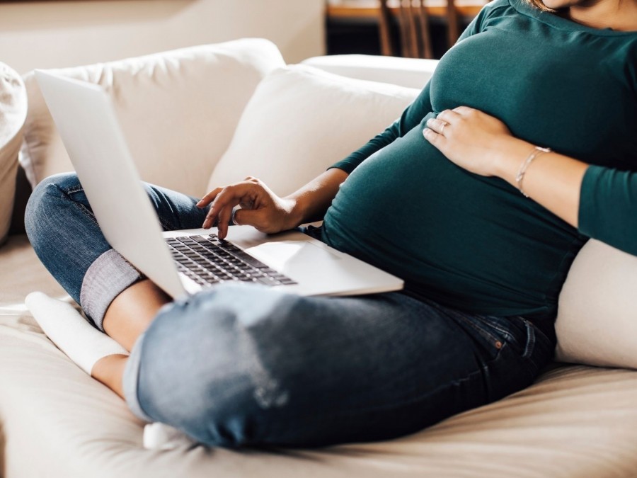 Schwangere sitzt mit Laptop auf dem Sofa und berechnet Fristen zum Mutterschutz. Fristenrechner, Geburtstermin, - Canva