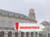 Im Hintergrund des Bildes ist das Historische Rathaus zu sehen. Im Vordergrund ein großer roter Schriftzug mit dem Wort Warnstreik und einem Ausrufezeichen.