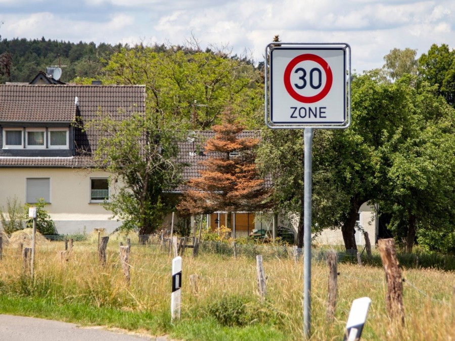 Tempo-30-Zonen Schild auf einer ländlichen Straße, zwei Wohnhäuser im Hintergrund, Anliegerstraße, verkehrsberuhigt, Erschließungssystem - Canva