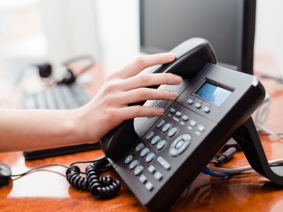 Hand greift zum Hörer eines Telefons auf einem Schreibtisch. Telefonhotline, Telefonberatung, telefonische Auskunft - Canva