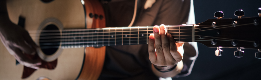 Das Bild zeigt einen Ausschnitt von einem Gitarrenspieler mit einer akustischen Gitarre. Es wird gerne für Veranstaltungen der Musikschule verwendet. - UnsplashGabrielGurrola