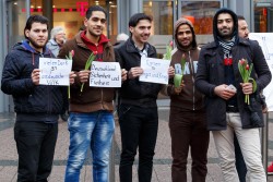 Flüchtlinge setzen Zeichen und suchen den Dialog: Bewohner der Flüchtlingsunterkunft auf dem Kirmesplatz an der Mintarder Straße verteilen Blumen vor dem Mülheimer Forum