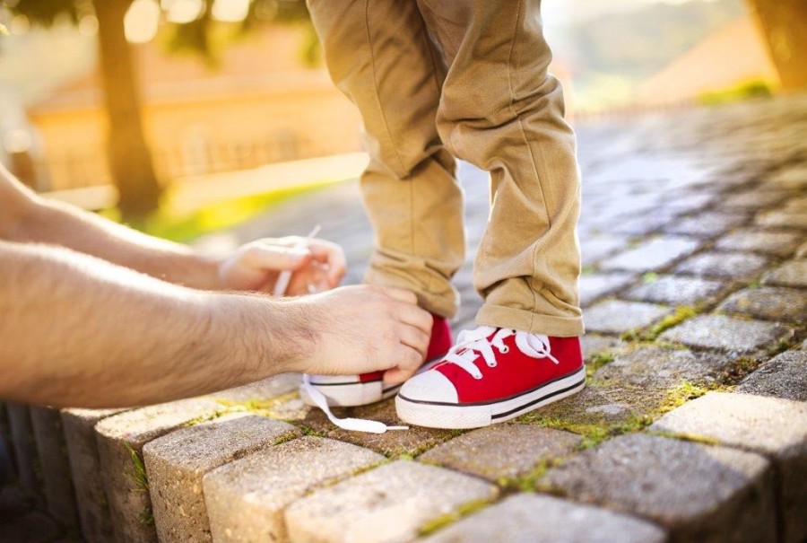 Erwachsener bindet einem Kind die Schuhe. In bestimmten Fällen kann dem Jugendamt die elterliche Sorge für minderjährige Kinder übertragen werden. Hierbei spricht man von Amtsvormundschaft und Amtspflegschaft.