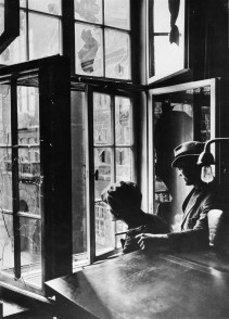 Zwei Angehörige der Rathauswache blicken durch ein zerschossenes Fenster auf die am Rathaus vorbeiführende Hindenburgstraße (heute Friedrich-Ebert-Straße). Links im Bild ist der Rathausturm erkennbar, April 1923. (Quelle: Stadtarchiv Mülheim an der Ruhr) - Stadtarchiv
