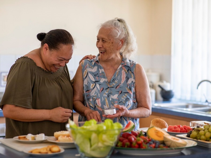 Betreuerin und ältere Dame kochen und lachen zusammen. Informationen zu Entlastung im Alltag bei der Haushaltsführung, Entlastung im Alltag durch individuelle Hilfen. Senioren, Seniorinnen - Canva