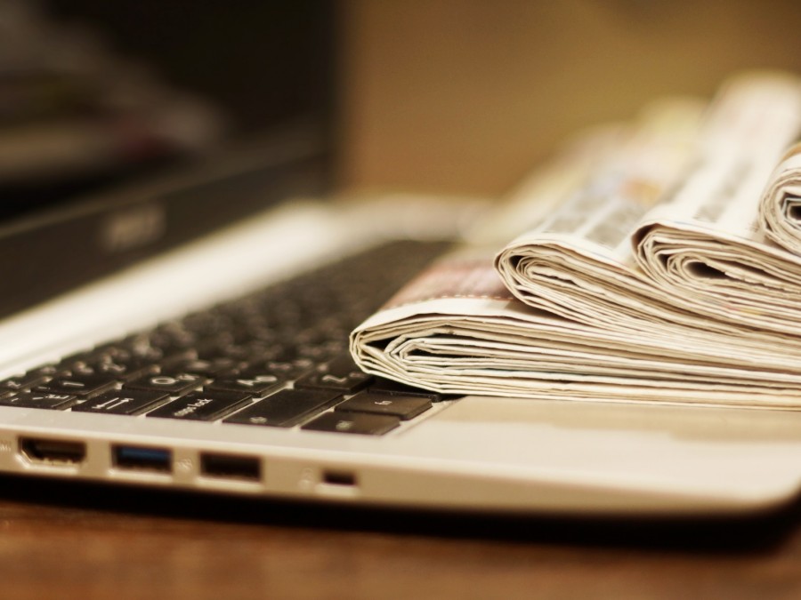 Pressearchiv, News, Artikelsammlung, Mitteilungen, Zeitungen, Medien, Aktuelle Pressemeldungen: Ein aufgeklappter Laptop,auf dem ein Stapel Zeitungen liegt. - Canva