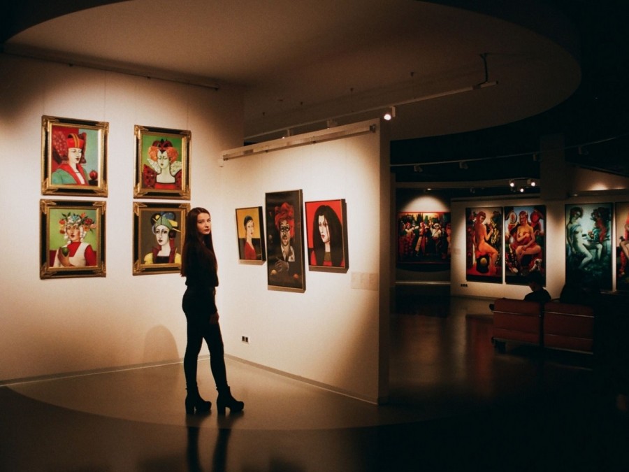 Besucherin einer Ausstellung schaut sich farbenfrohe gemalte Bilder an. INfos zur Anmeldung von Ausstellungen. - canva