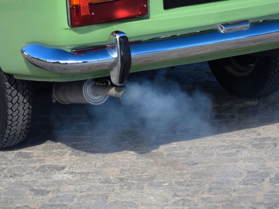 Bildausschnitt mit Teil eines grünen Autos mit Auspuff, Stoßstange und Hinterreifen. Abgase, Feinstaubplaketten, Umweltzonen - Canva