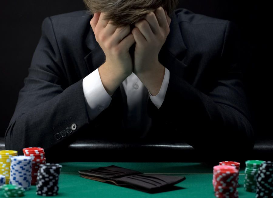 Mann am Pokertisch, mit Pokerchips und leerer Brieftasche, versteckt sein Gesicht verzweifelt hinter seinen Händen. Türkische Beratungshotline für Glücksspielsucht. - Canva.com