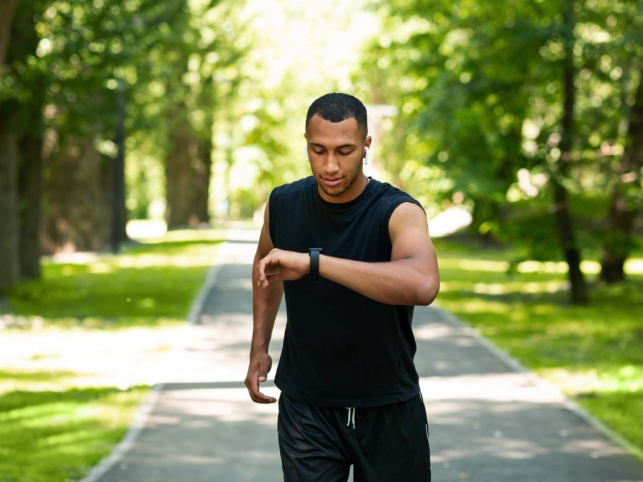Sportler beim Lauftraining kontrolliert seine Pulsuhr, Smartwatches, Digitalisierung im Sport, Fitnesstracker, Sportstudios, Sportvereine - Canva