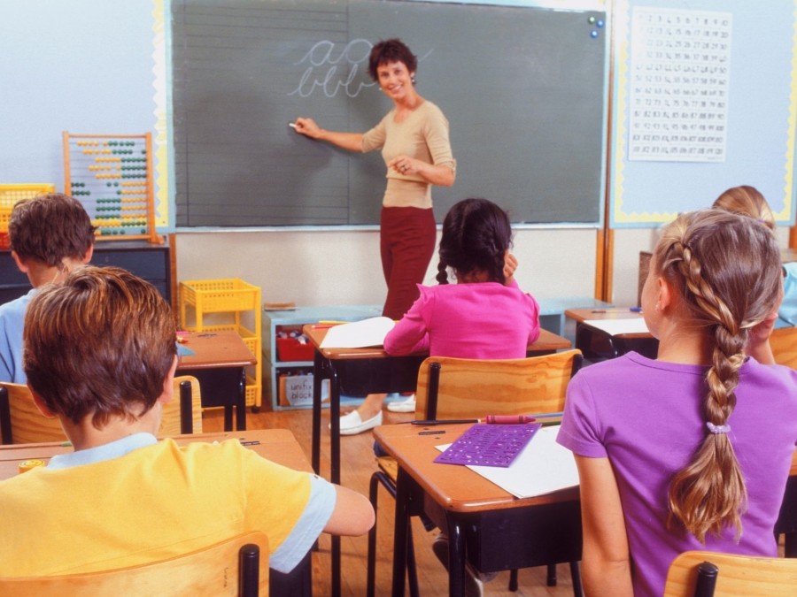 Lehrerin vor der Tafel im Klassenzimmer erklärt Grundschulkindern das ABC. Einschulung, Grundschulen, Schulwahl - Canva