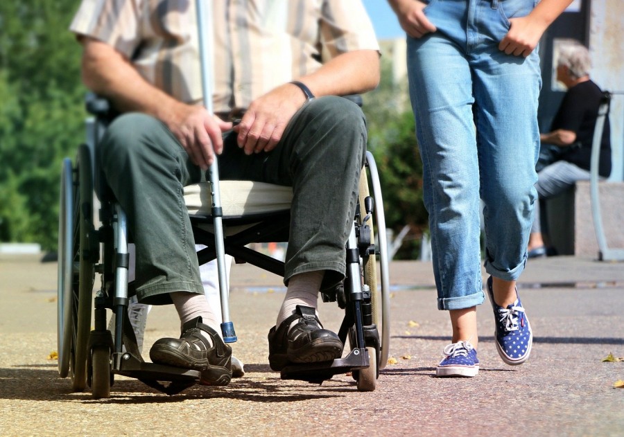 Bildausschnitt zeigt Szene aus einem Spaziergang, männliche Person im Rollstuhl, daneben läuft eine junge Frau. Personen mit einer anerkannten Schwerbehinderung können bereits vor dem 67. Lebensjahr ohne eine Kürzung Rente beziehen. - Bild von klimkin auf Pixabay