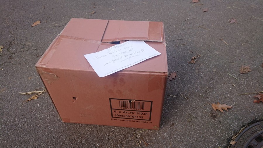 Das Foto zeigt einen roten Karton mit einem weißen Zettel oben auf, auf dem steht: Ein Geschenk Diese Tauben sind zu wertvoll um getötet zu werden - Karin Braun