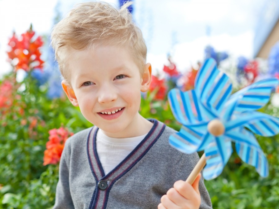 Das Bild zeigt einen kleinen lachenden Jungen im Garten, der ein Windrad in der Hand hält. - Canva