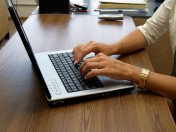 Hände und Unterarme einer Person vor einem aufgeklappten Laptop an einem Tisch. Online Befragung, Homeoffice Notebook, 