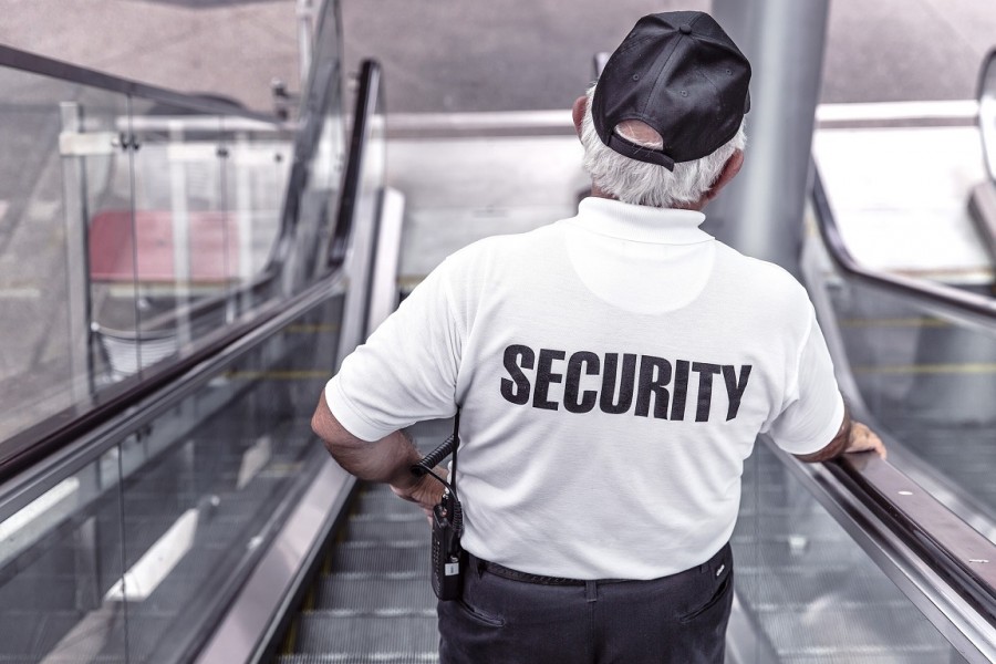 Wachmann mit der Aufschrift Security auf dem Rücken auf einer Rolltreppe. Infos zum Bewachungsgewerbe. - Pixabay