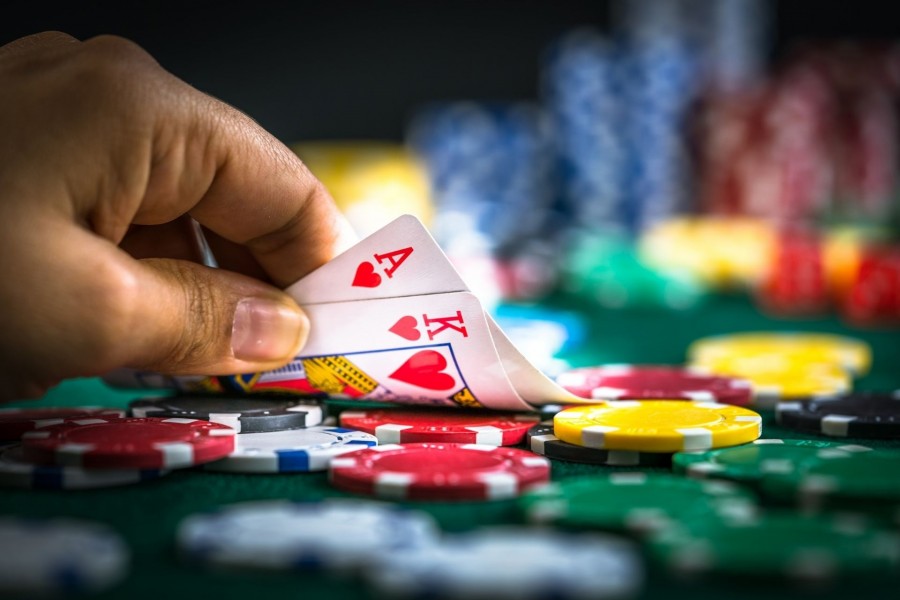 Pokertisch mit Coins und einer Hand, die eine Herz-Ass und Herz-König Spielkarte aufdeckt. Pokern, Pokerturnier, Chips - Canva