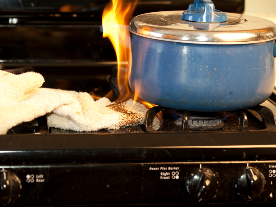 Brennendes Küchenhandtuch, das an einem Gasherd mit blauem Topf Feuer gefangen hat. Infos zu Brandgefahren im Haushalt. - Canva