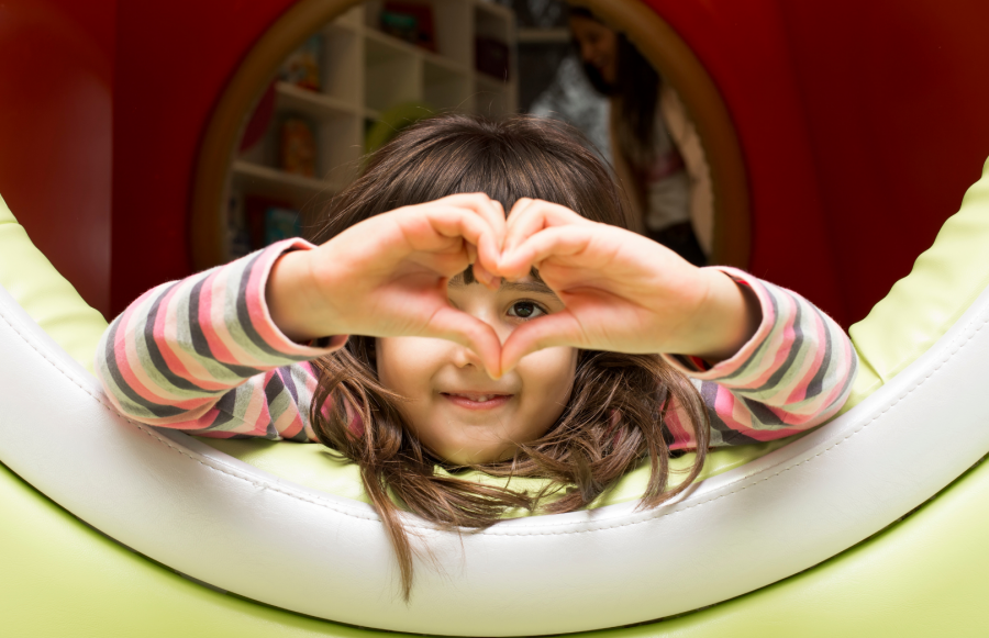 Kleines Mädchen liegt in einer Spielhöhle und formt mit ihren Händen ein Herz. Kindertagespflege - Canva.com