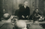 Der von der britischen Militärregierung wieder eingesetzte Oberbürgermeister Hoosmann spricht zwischen britischen Offizieren zum Bürgerausschuss. (1945) - Quelle/Autor: Stadtarchiv