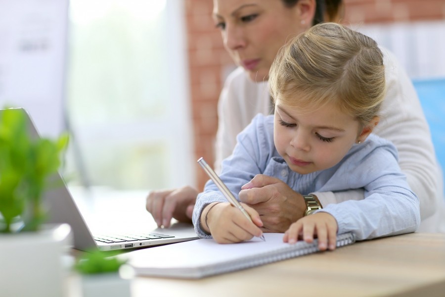 Mutter arbeitet am Laptop mit dem Kind auf dem Schloß. Wer Familie und Beruf miteinander vereinbaren möchte, muss viele Herausforderungen meistern. - shutterstock